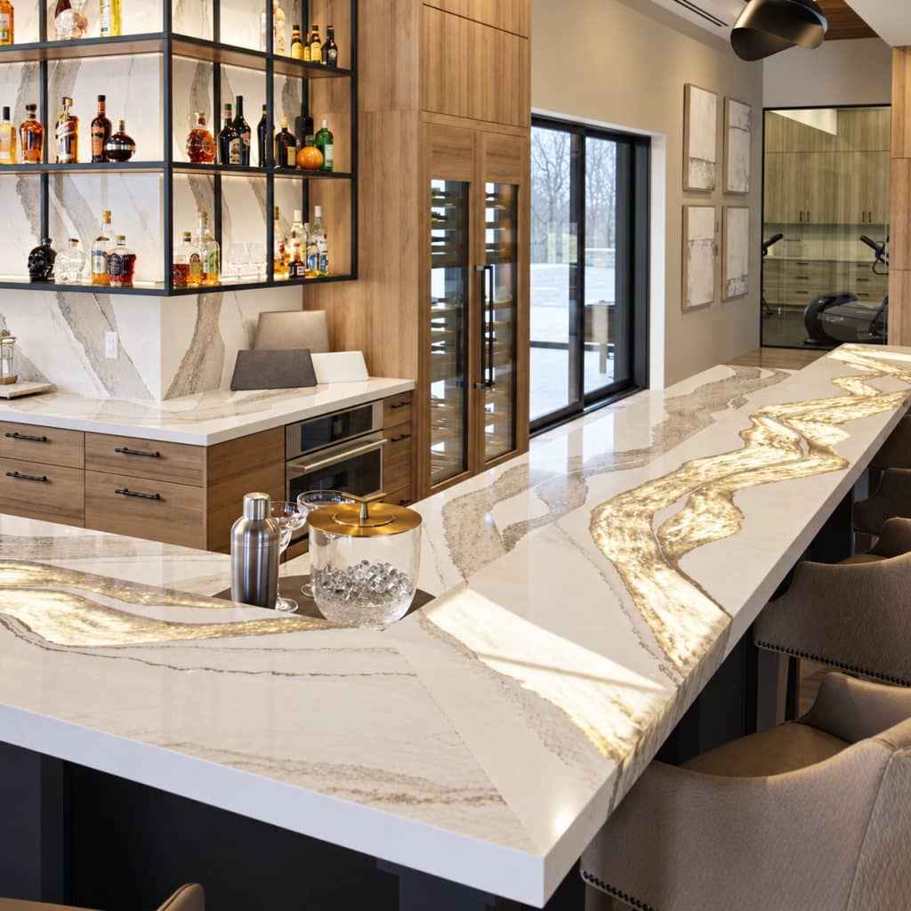 Modern home bar featuring a long, white quartz countertop with dramatic, backlit gold and gray veins glowing from within.